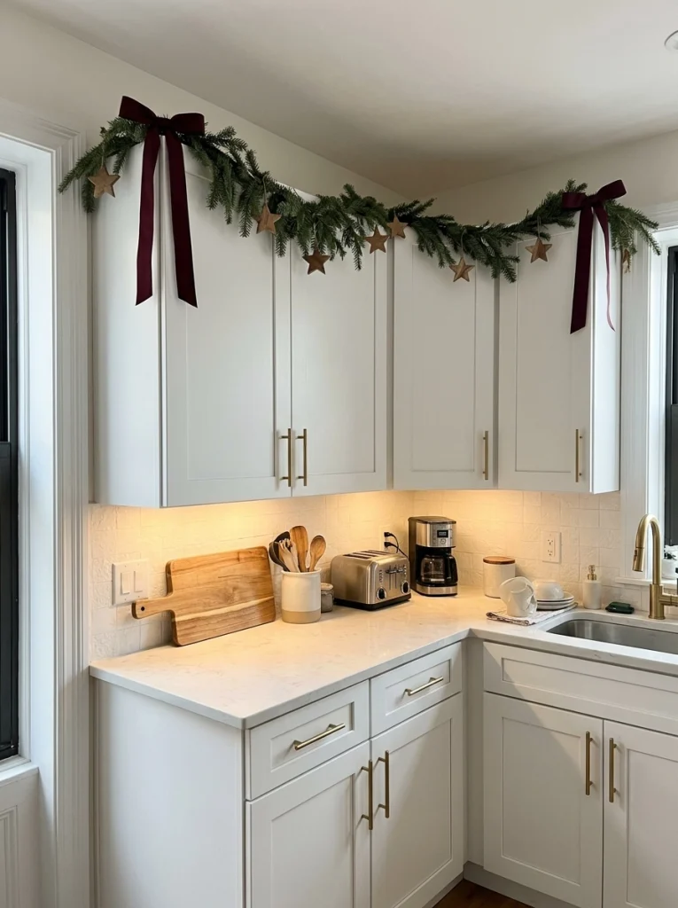 A short evergreen garland adds Christmas color above apartment kitchen cabinets.