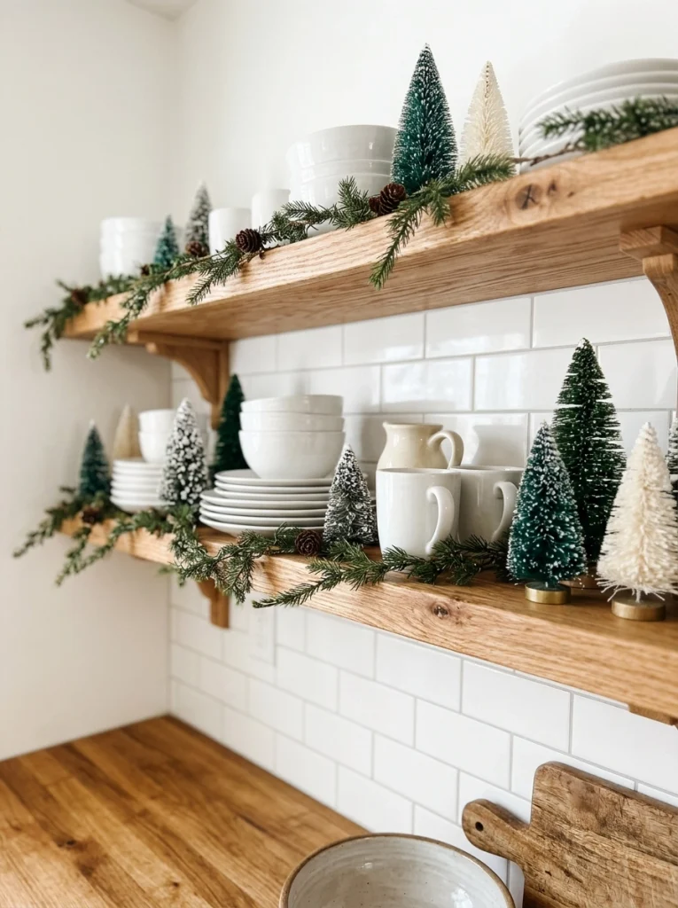 Farmhouse Christmas kitchen decor with miniature trees, white dishes, and natural wood shelves.
